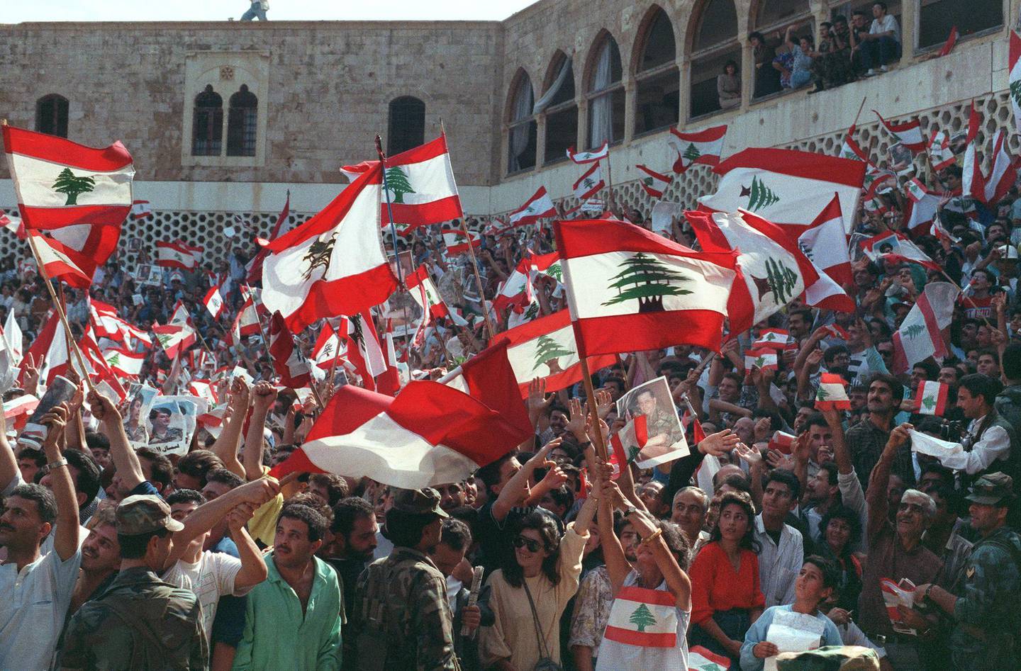 Christian Lebanese people wave national flags and portraits of General Aoun while they stage a protest 04 November 1989 in front of Baabda presidential palace in East Beirut against agreement reached in October by deputies and the Arab League Committee in Taif.  After a month of intense discussion, in October 1989, the deputies informally agreed on a charter of national reconciliation, also known as Taif agreement. General Aoun, claiming powers as interim Prime Minister, issued a decree in early November dissolving the parliament and did not accept the ratification of the Taif agreement. The Lebanese civil war broken out in April 1975. AFP PHOTO JOSEPH BARRAK (Photo by JOSEPH BARRAK / AFP)