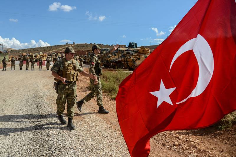 Turkish soldiers stand near armoured vehicles as a man waves a Turkish national flag during a demonstration in support of the Turkish army's Idlib operation near the Turkey-Syria border near Reyhanli, Hatay, on October 10, 2017.
The Turkish army has launched a reconnaissance mission in Syria's largely jihadist-controlled northwestern Idlib province in a bid to create a de-escalation zone, the military said on October 9.  / AFP PHOTO / ILYAS AKENGIN