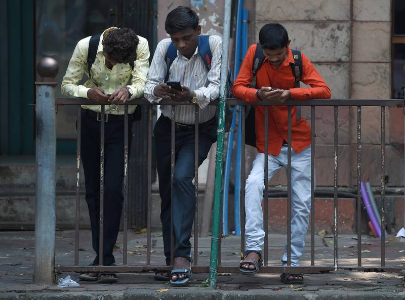 Indian men check their smartphones outside the Bombay Stock Exchange (BSE) in Mumbai on October 11, 2018. (Photo by Indranil MUKHERJEE / AFP)
