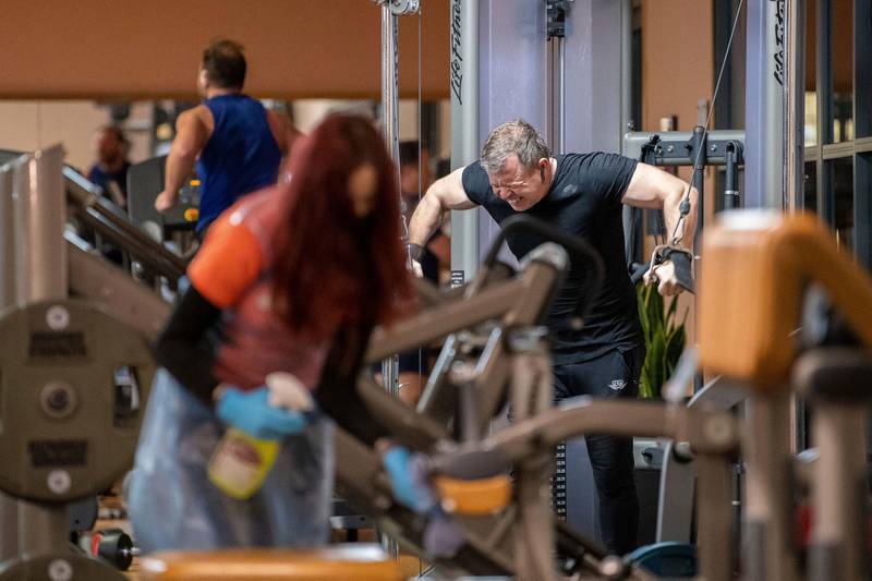A member of staff cleans gym equipment as gym members return to work out at David Lloyd health club in Leicester. AP Photo