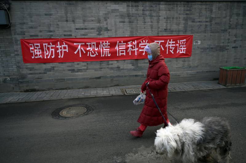 A woman with a face mask walks a dog past a banner on a wall in Beijing, China. Reuters