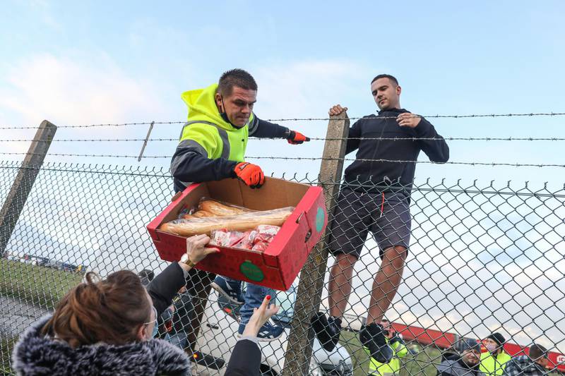 A volunteer scales a fence to distribute a carton of fresh food to a truck driver at Manston airport in Manston, U.K. Routes to Dover, Britain's busiest cross-channel port, have been choked for days after France shut its border with Britain, blaming an outbreak of a novel strain of the coronavirus. Bloomberg