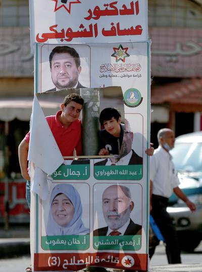 Youths pose for a picture through a tear in a campaign poster of candidates for the upcoming Jordanian parliamentary elections line a street in the capital Amman. AFP