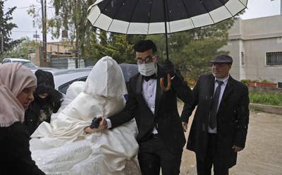 Palestinian groom Imad Sharaf, wearing gloves and a face mask, accompanies his bride Bara'a Amarneh as they arrive at their home in the village of al-Dahriya, south of Hebron in the West Bank, on March 20, 2020. AFP