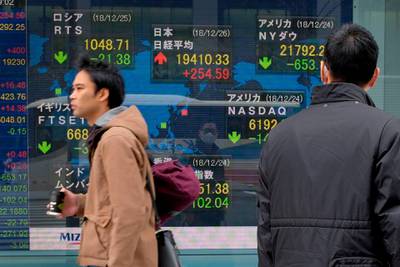 Pedestrians walk past a stock indicator board showing the share price of the Tokyo Stock Exchange (C) in Tokyo on December 26, 2018. Tokyo stocks opened higher on December 26, rebounding from the previous day's five percent drop as the yen's rise took a breather. / AFP / Kazuhiro NOGI
