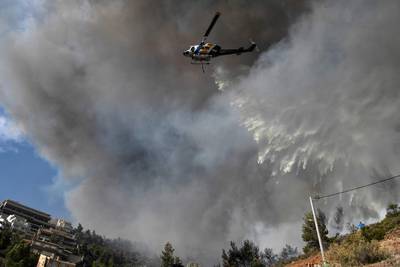 A helicopter drops water on a bushfire near a residential district in Athens. The fire forced residents to flee. AFP