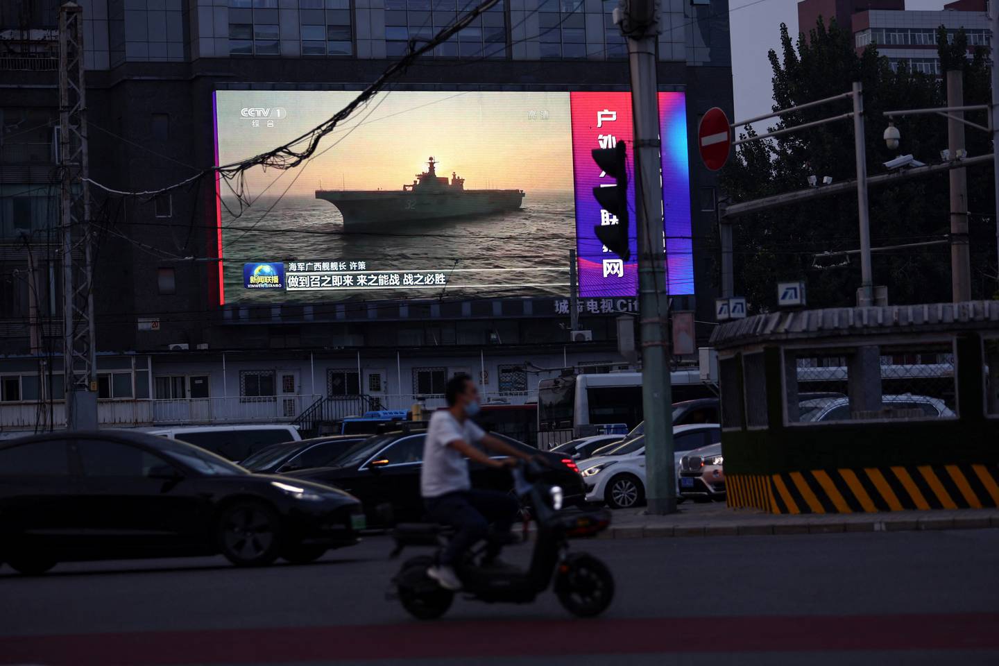 A man rides a scooter past a screen showing footage of a Chinese People's Liberation Army ship during an evening news programme in Beijing, China. Reuters
