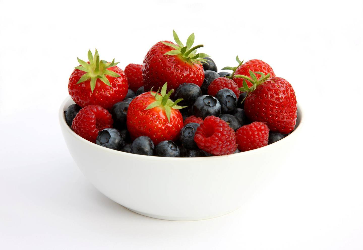 White bowl filled with newly picked home grown, organic strawberries, raspberries and blueberries, on a white background.