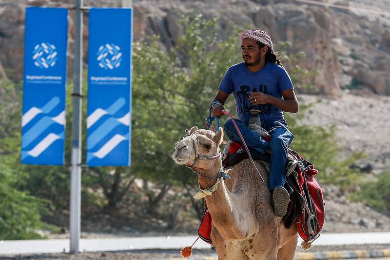 A man rides a camel along a road past signs bearing the name and logo of the conference in Sweimeh. AFP