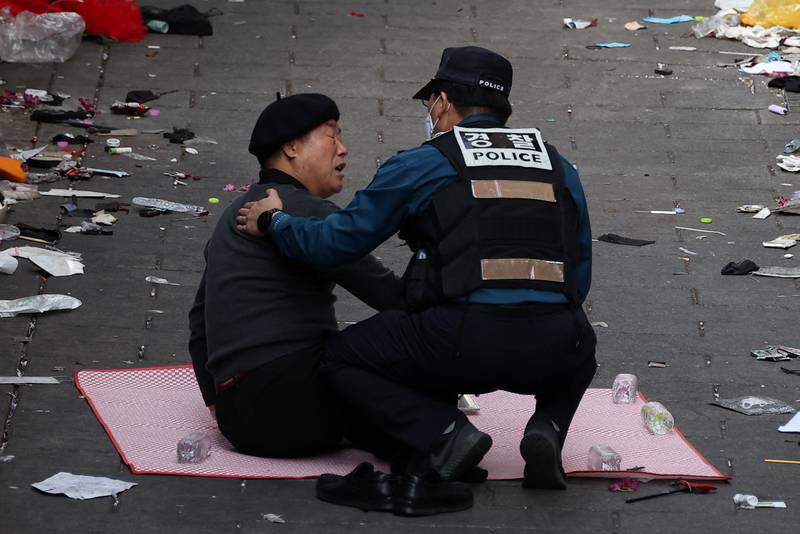 A police officer attempts to move a man as he pays tribute at the site. Reuters