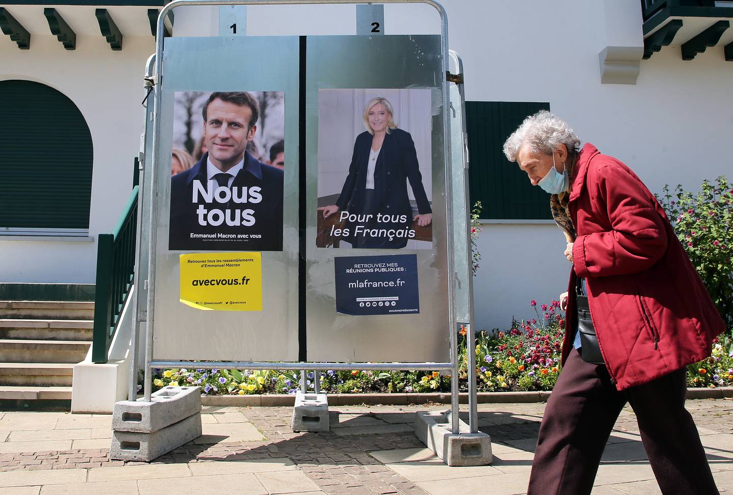 A woman walks past presidential campaign posters of French President and centrist candidate for reelection Emmanuel Macron and French far-right presidential candidate Marine Le Pen in Anglet, south-western France, Saturday, April 16, 2022.  France will vote on Sunday April 24 in the second round of the presidential election. AP