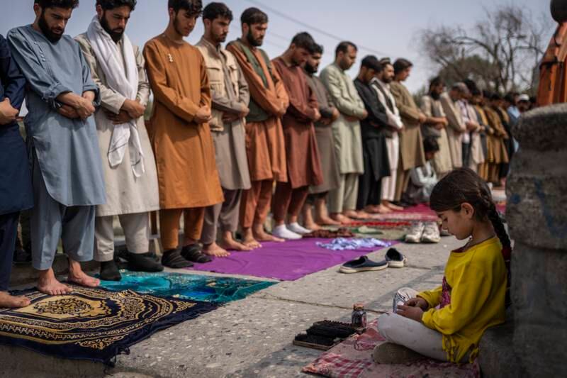 An Afghan girl working as a shoe cleaner sits in the street while men pray. Photo: AP