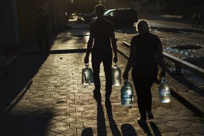 A couple carry water bottles after filling them up at a store in Pokrovsk, Donetsk region. AP