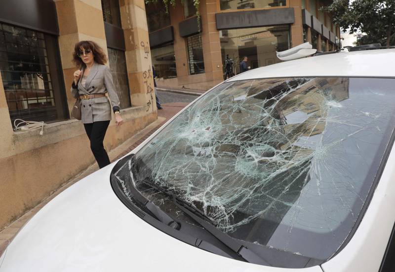 A Lebanese woman walks by a damaged car after a night of clashes between supporters of the Shiite groups Hezbollah and Amal and anti-government demonstrators in the capital Beirut. AFP
