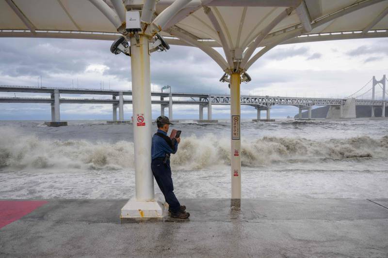A man takes pictures of waves crashing into a promenade in Busan. AFP