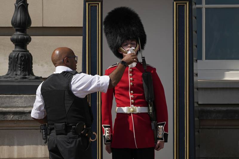 A soldier outside Buckingham Palace is given water by a police officer on Monday, as temperatures soared across the country. AP