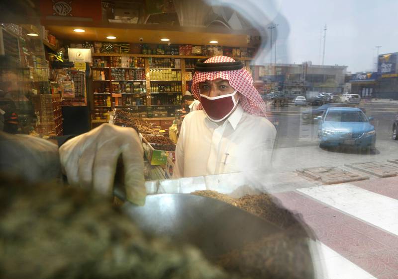 A man wearing a face mask as a precaution against the spread of the coronavirus is reflected in the window of a store as he buys herbs in Jiddah. AP