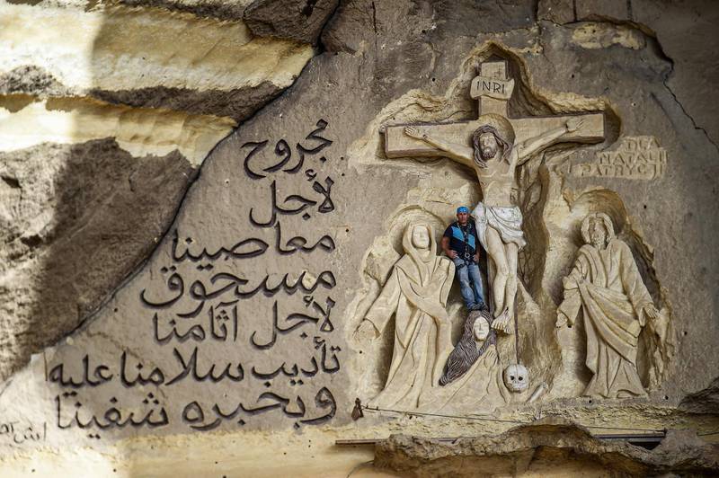 Polish artist Mario, sculptor of St. Simon the Tanner Monastery complex, poses for a picture alongside a scene relief depicting the Crucifixion of Jesus Christ and a verse in Arabic from the Biblical Book of Isaiah reading "he was wounded for our transgressions, he was bruised for our iniquities, the chastisement of our peace was upon him; and with his stripes we are healed", at the church in the Egyptian capital Cairo's eastern hillside Mokattam district, . Mario spent more than two decades carving the rugged insides of the seven cave churches and chapels of the rock-hewn St. Simon Monastery and church complex atop Cairo's Mokattam hills, with designs inspired by biblical stories. It was all done to fulfil the wishes of the church's parish priest who met Mario in the early 1990s in Cairo. The Polish artist, who had arrived in Egypt earlier on an educational mission, was then looking for an opportunity to serve God at the monastery.  AFP