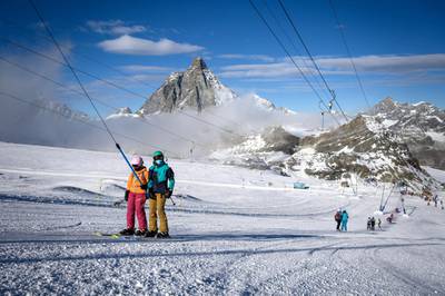 Skiers wearing protective face masks ride a ski lift before hitting the slopes with the Matterhorn mountain as landscape above the ski resort of Zermatt in the Swiss Alps on November 28, 2020. - In non-EU Switzerland, which has been hard-hit by the second wave of Covid-19, the authorities, ski and tourism sectors have stood united behind the decision to keep the winter season going as EU countries debate a bloc-wide ban on ski holidays to curb coronavirus infections. "In Switzerland, we can go skiing, with protection plans in place," Swiss Health Minister Alain Berset told reporters on November 26, 2020. (Photo by Fabrice COFFRINI / AFP)