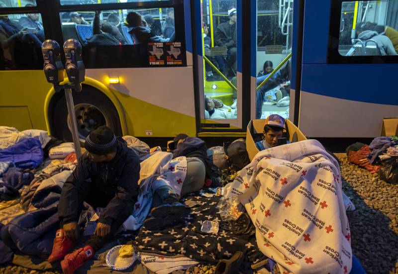 Migrants prepare to spend the night on the pavement or inside an idle city bus as they attempt to stay warm. AP