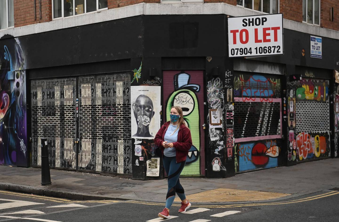 epa08740397 A masked woman passes a closed shop in the Tower Hamlet area of London, Britain, 13 October 2020. The UK unemployment rate rose to 4.5 percent between June and August as the pandemic continued to hit jobs.  EPA/NEIL HALL