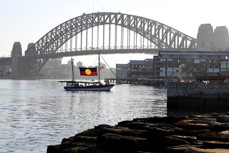 The ceremonial flame arrives by a boat bearing the Australian Aboriginal flag during the Australia Day Wugulora Morning Ceremony on the Walumil Lawns at Barangaroo in Sydney, Australia.  Protests across Australia called for a change in the date of the holiday. EPA