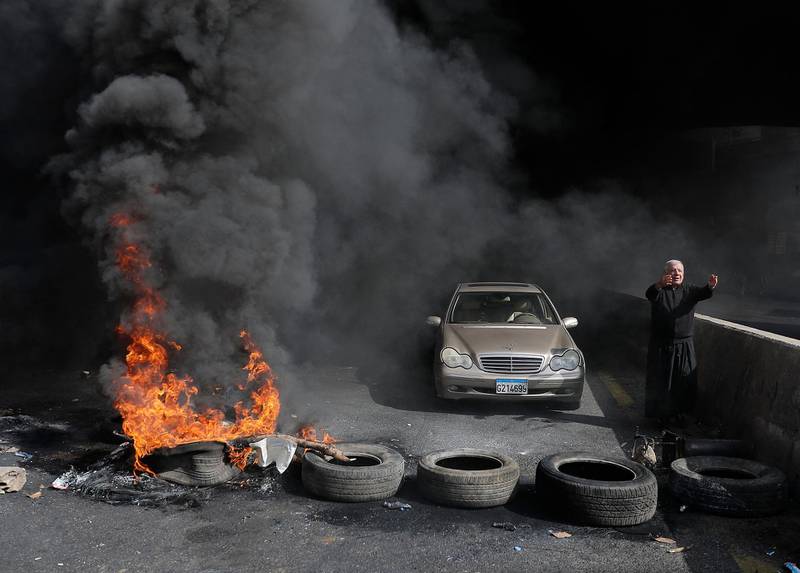 A Maronite priest pleads with anti-government protesters to let him pass with his vehicle as he stands next to burning tyres at a makeshift roadblock in Zouk Mosbeh, north of Lebanon's capital Beirut. AFP