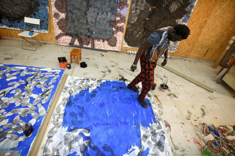 Senegalese artist Omar Ba walks over a large canvas while wearing ink-dipped sandals at his studio in March. Cooper Inveen / Reuters