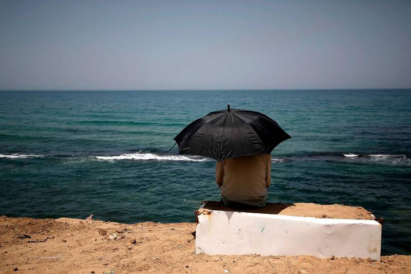 A Palestinian sits beneath an umbrella by the shoreline of a beach in Gaza City. AFP