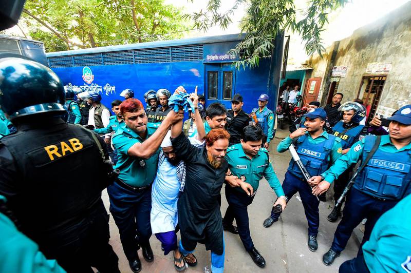 Police escort detainees (C) accused of allegedly plotting the Holey Artisan Bakery cafe attack, carried out by Islamist militants, to a courtroom for their trial in Dhaka on November 27, 2019. Five young men armed with guns and knives stormed the cafe on July 1, 2016 taking dozens hostage and killing 22 people. / AFP / Munir UZ ZAMAN
