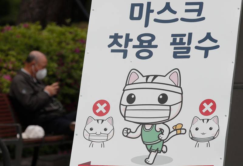 A man looks at his smartphone near a banner reading "Mandatory mask wearing" at a park in Goyang, South Korea. AP Photo