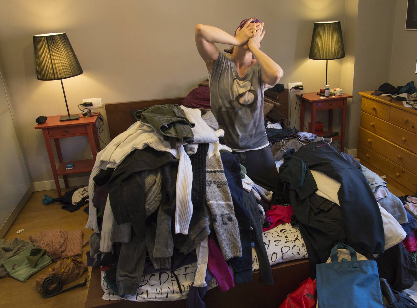 Wide angle view of young woman with hands covering face kneeling on bed among large tiles of clothes and other objects in a chaotic bedroom. León, Castilla y León, Spain. Getty Images