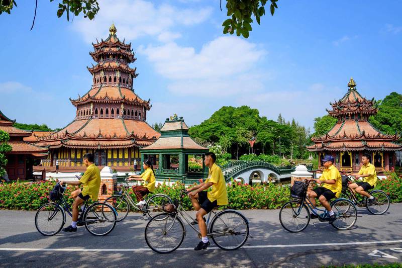 Schoolchildren ride bicycles past a replica of the Phra Kaew Pavilion in the Ancient City Heritage Park in Samut Prakan, some 25km south of Bangkok on December 9, 2020. / AFP / Mladen ANTONOV

