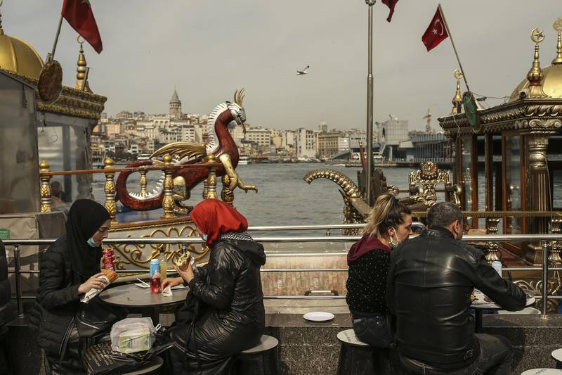People enjoy a snack by the Golden Horn in Eminonu open market in Istanbul, Friday, April 2, 2021. The number of confirmed COVID-19 cases in Turkey continue to raise and the total number of infections in the country stands at 3.3 million. On Monday, Turkish President Recep Tayyip Erdogan's government re-imposed restrictions, including weekend lockdowns, amid a sharp increase in the number of infections-less then a month after the measures were relaxed. The government has also announced restrictions over the upcoming Muslim holy month of Ramadan. (AP Photo/Emrah Gurel)