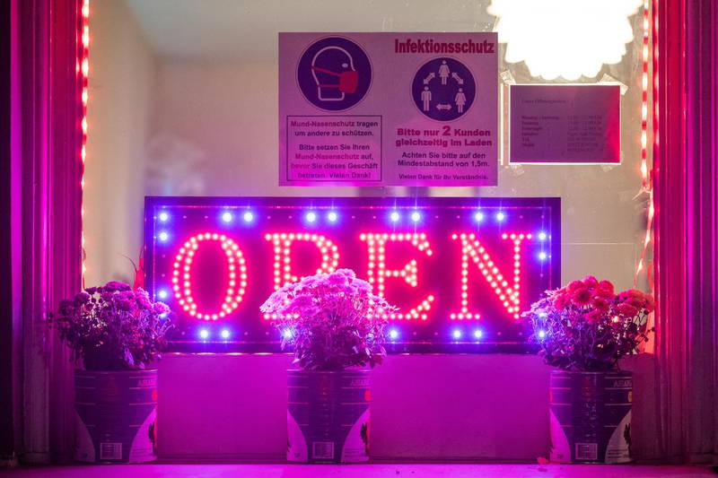 A neon sign reading 'Open' is seen on a window of a closed restaurant with a placard reading 'Wear a nose and mouse protection to protect others. Please only 2 customers in the shop at the same time' in Berlin, Germany.  EPA