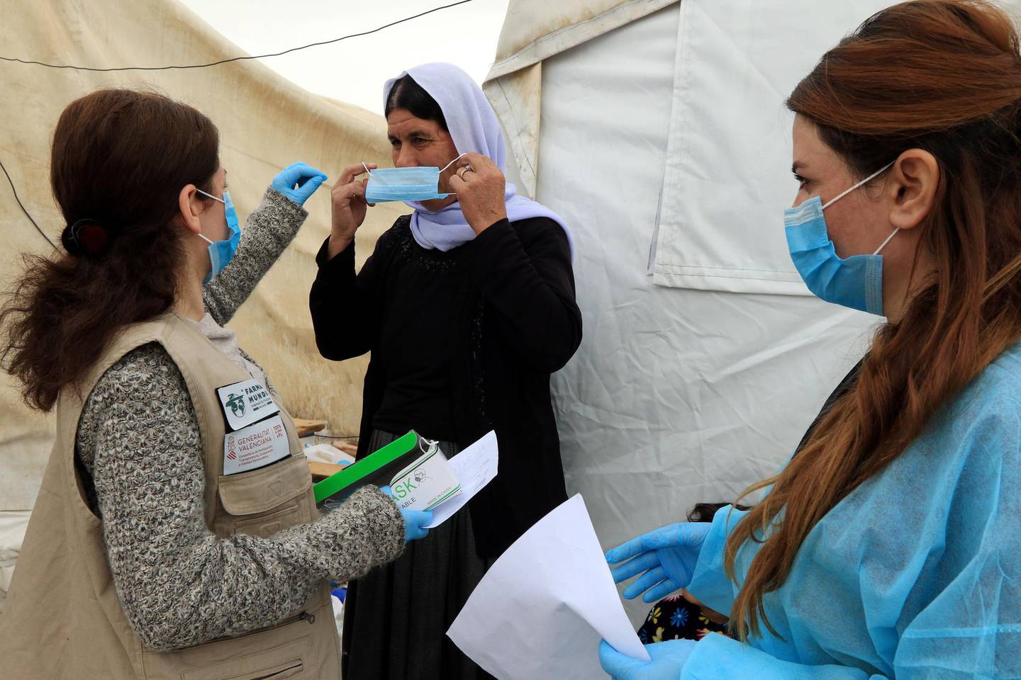 A member of medical staff, assists a Yazidi displaced woman to wear a protective face mask, following the coronavirus outbreak, at the Sharya camp in Duhok, Iraq March 7, 2020. REUTERS/Ari Jalal