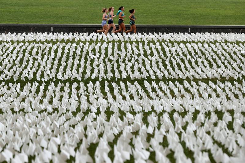 WASHINGTON, DC - SEPTEMBER 17: Runners pass 'In America: Remember,' a public art installation commemorating all the Americans who have died due to COVID-19 near the Washington Monument on September 17, 2021 in Washington, DC.  The concept of artist Suzanne Brennan Firstenberg, the installation includes more than 660,000 small plastic flags, some with personal messages to those who have died, planted in 20 acres of the National Mall.    Chip Somodevilla / Getty Images / AFP
