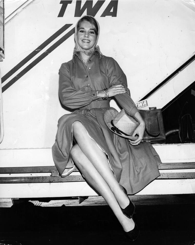Jane Fonda, in a trench coat with a headscarf and straw hat, waits to board a TWA Jetliner from New York to Los Angeles on November 16, 1962.