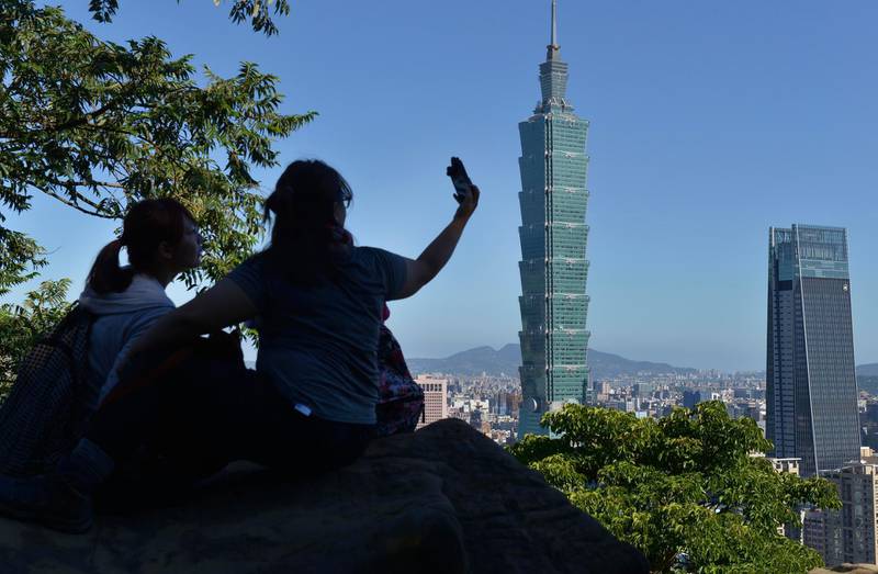 People take a selfie at Elephant Mountain before Taipei 101 Tower (C) and Nan Shan Tower (R) in Taipei on July 14, 2018. (Photo by Chris STOWERS / AFP)