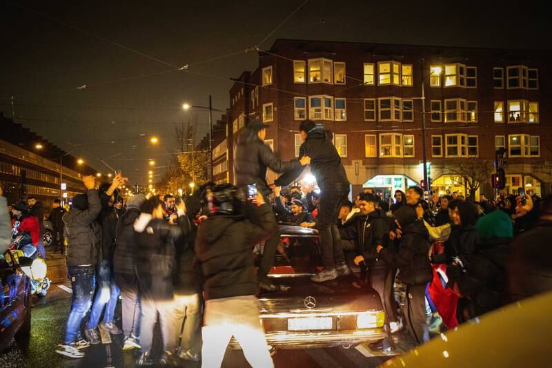 Fans climb on to a car following the Morocco victory, in Amsterdam. EPA