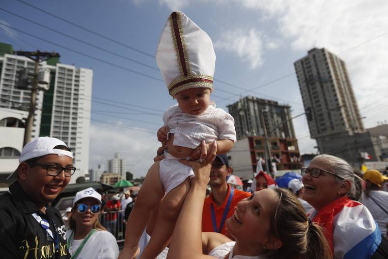 A woman holds a baby wearing a miter as they await the arrival of Pope Francis in Panama City. EPA
