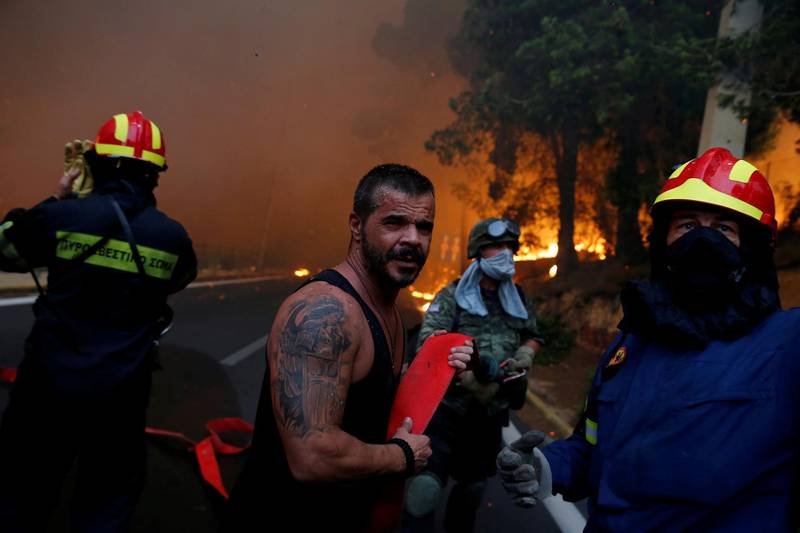 Firefighters, soldiers and local residents carry a hose as a wildfire burns in the town of Rafina, near Athens. Reuters