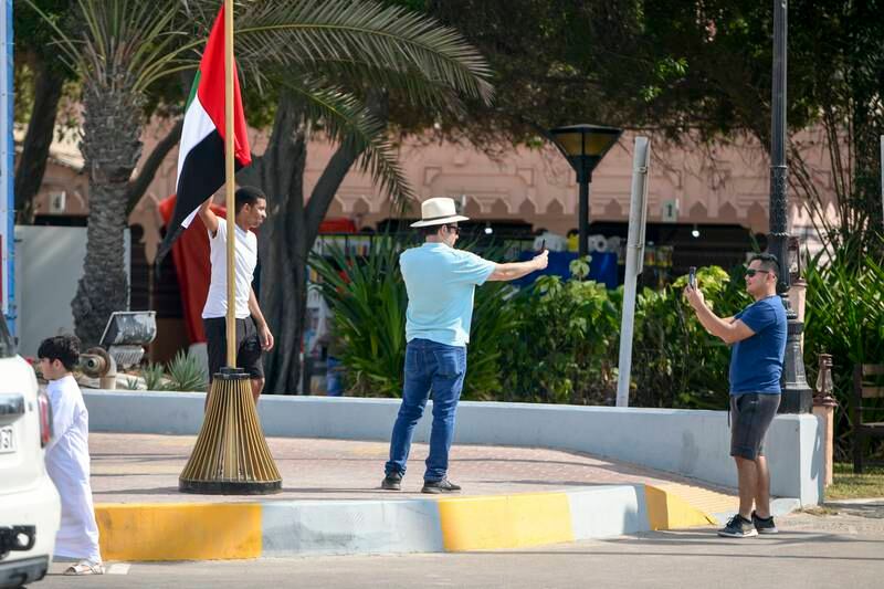 Tourists take photos by a UAE flag at Abu Dhabi Corniche. Khushnum Bhandari / The National

