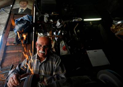 A Syrian man works in his metal workshop beneath a portrait of Syrian President Bashar al-Assad in old Damascus, on June  16, 2020. The Caesar Syria Civilian Protection Act of 2019, a US law that aims to sanction any person who assists the Syrian government or contributes to the country's reconstruction, is to come into force on June 17. / AFP / LOUAI BESHARA
