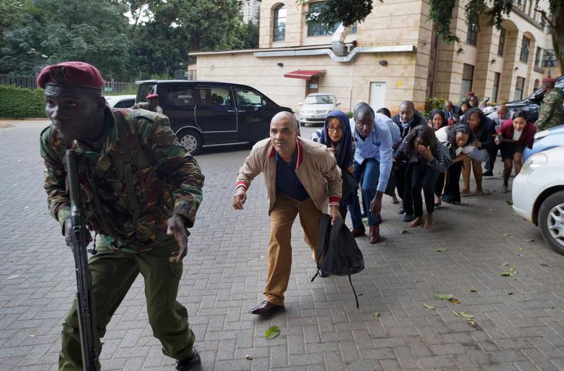 Civilians who had been hiding in buildings flee under the direction of a member of security forces at a hotel complex in Nairobi, Kenya Tuesday, Jan. 15, 2019. Terrorists attacked an upscale hotel complex in Kenya's capital Tuesday, sending people fleeing in panic as explosions and heavy gunfire reverberated through the neighborhood. (AP Photo/Ben Curtis)