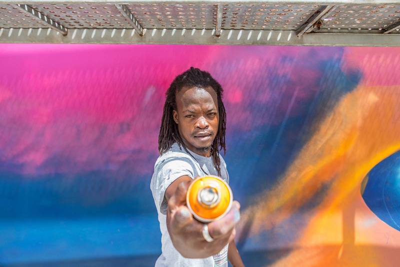 Beninese artist Laurenson Djihouessi, also known as Mr Stone, poses with a spray can in hand at the site of Effet Graff festival, whose objective is to achieve one of the longest murals in the world, in Cotonou on May 18, 2022.  - 26 Beninese and international graffiti artists are taking part in the eighth edition of the Effet Graff festival in Cotonou, with the ambition of creating one of the largest murals in the world that traces the history and culture of Benin.  The fresco pays tribute in particular to the 26 Beninese treasures looted by French colonial troops and returned to Benin in November 2021, and the theme of this edition is a "new Benin".  (Photo by YANICK FOLLY  /  AFP)