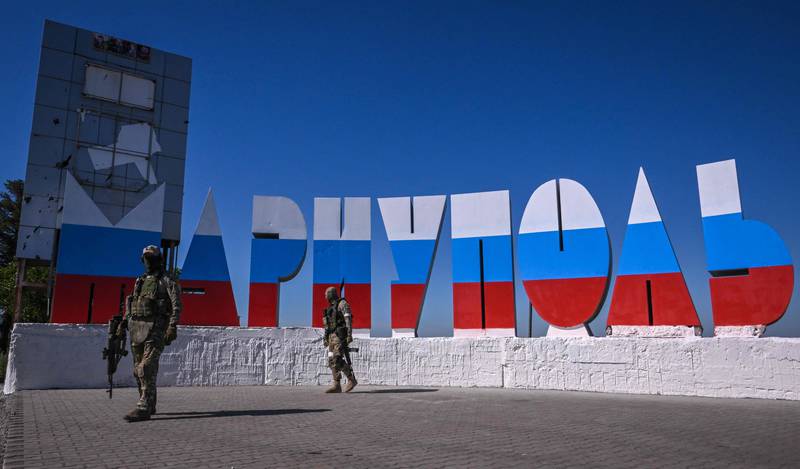 Russian soldiers walk near a monument at the entrance of Mariupol, which has been painted in the colours of the Russian flag. AFP