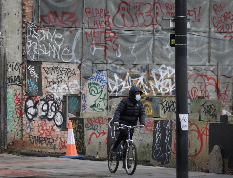 A cyclist wears a mask as he passes graffiti in London during England's third national lockdown. AP Photo