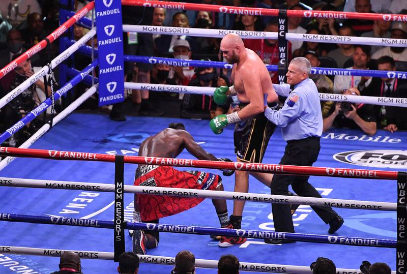 Deontay Wilder goes down on one knee as the referee holds  back Tyson Fury during round six. AFP