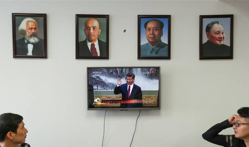 Framed portraits of German philosopher Karl Marx, Soviet state founder Vladimir Lenin and China's late leaders Mao Zedong and Deng Xiaoping hang above a screen showing a news broadcast of China's President Xi Jinping attending a meeting in Beijing. Stringer / Reuters